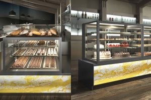 A modern bakery display case filled with assorted breads, pastries, and cakes, set in a bright, stylish shop with wooden floors and illuminated shelves in the background.
