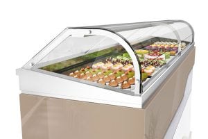 A refrigerated display case filled with assorted pastries, cakes, and desserts behind a curved glass cover, set against a white background.