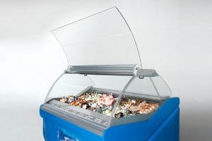 A blue commercial ice cream display freezer with a curved glass lid open, showing various flavors of ice cream and toppings inside against a plain light background.