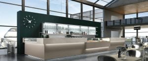 A modern airport café with sleek counters, display cases of food, a large wall clock, and glass shelves holding bottles. Large windows and natural light fill the space; a plane is visible outside.