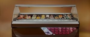 A display case filled with various flavors of gelato, each topped with colorful and decorative ingredients, set against a brown background with a chocolate bar graphic on the front.