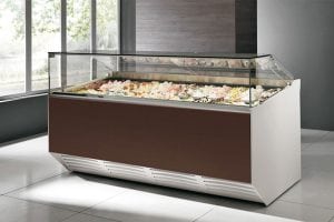 A modern gelato display case filled with various colorful flavors of gelato, located in a bright room with large windows and tiled floors.