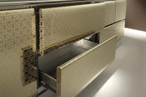 Close-up of modern kitchen cabinets with glossy gold geometric patterns, featuring several drawers partially open, revealing metallic interiors. The design is sleek and contemporary.