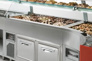 A display case filled with assorted cookies and pastries in a self-service bakery or dessert shop, with trays neatly arranged under a glass cover.