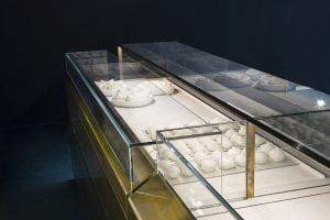 A modern glass display case with metal edges contains plates of white, round balls of dough, possibly cheese or bread, set against a dark background.