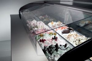 A display case filled with various flavors of gelato, featuring colorful toppings like berries, chocolate, and nuts under a glass cover.