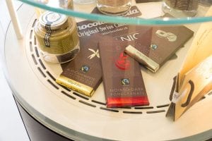 A glass display case showing various chocolate bars, including dark and white chocolate with Fairtrade and organic labels, and a jar of spread. The bars are partially stacked and arranged neatly.