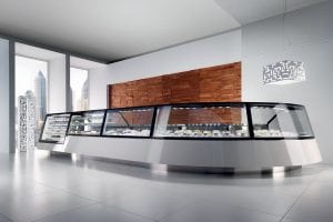 A modern gelato display case with glass panels in a minimalist, bright shop interior with large windows, city skyline view, white floors, a wood accent wall, and a geometric pendant light.