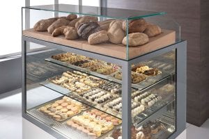 A bakery display case with loaves of bread on top and shelves below filled with assorted pastries, cookies, and desserts, all neatly arranged behind glass.