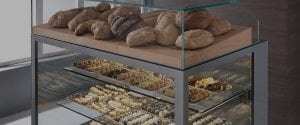 A bakery display case with assorted loaves of bread on the top shelf and trays of various pastries and cookies arranged on lower glass shelves.