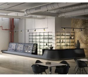 Modern café interior with industrial-style decor, black furniture, glass display cases with pastries, open shelving with dishes, exposed pipes, and a large abstract wall art. Empty tables and chairs are in the foreground.