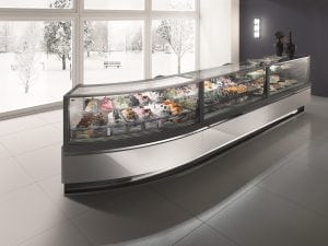 A modern glass display case filled with assorted gelato sits in a bright, minimalist room with large windows showing a snowy landscape and trees outside.
