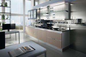 Modern kitchen with light wood cabinets, stainless steel appliances, glass shelves holding glassware, large windows with city view, and a table with an open book in the foreground.