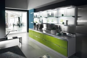 Modern kitchen with glossy green lower cabinets, stainless steel countertop, open glass shelves holding bottles and glassware, and large window overlooking a bright, spacious lobby area. Minimalist decor and sleek design.