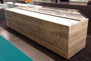 A modern display case with a wooden base and glass top, designed for showcasing items. The case is empty and is situated in an indoor exhibition or retail space.