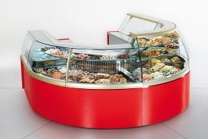 A curved, red display case with glass panels showcases a variety of pastries, cookies, and baked goods arranged on multiple shelves in a bakery or cafe setting.