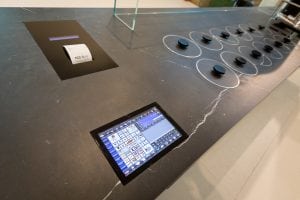 A modern kitchen countertop with a built-in touchscreen control panel, black burner knobs, and a digital display screen, all integrated into a sleek, dark surface.