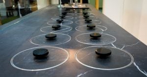 A row of modern black induction cooktops with round cooking zones and black control knobs, set into a dark countertop with white veining in a contemporary kitchen setting.