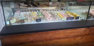 A glass display case shows colorful decorated cookies and rows of assorted macarons with labels for flavors like vanilla bean, passion fruit, and berries, along with price tags of $3 and $7.