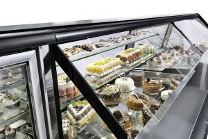 A glass display case filled with a variety of cakes, pastries, and desserts, including layered cakes, tarts, and macarons, arranged neatly on shelves in a bakery or patisserie.