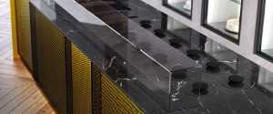 A modern kitchen countertop made of black marble with white veining, featuring a sleek glass divider and minimalist black stovetop burners, with yellow textured cabinet panels below.
