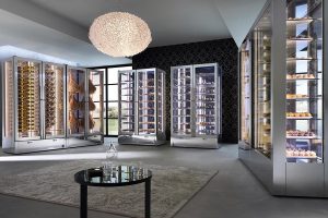 A modern, luxurious bakery with glass display cases filled with bread and pastries, a round table and decorative rug in the center, and a large, elegant chandelier hanging from the ceiling.