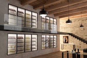 Modern wine cellar with glass-fronted shelves displaying rows of red and white wine bottles, exposed brick walls, wooden beams on the ceiling, and contemporary lighting fixtures. A staircase and a wine-themed artwork are visible.