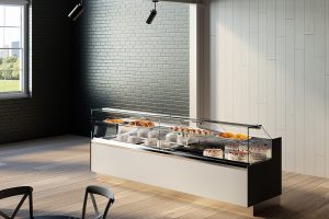 A modern bakery display case with various pastries, cakes, and desserts inside, set in a bright room with black and white walls, wooden flooring, and overhead lighting.