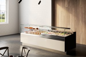 A modern gelato and pastry display case in a bright room with a white brick wall, wooden accent wall, and large window. The case contains assorted gelato flavors and desserts.