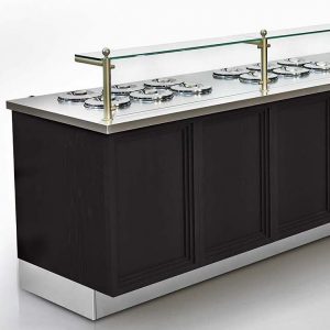 A modern gelato display counter with a dark wood base, stainless steel top, glass sneeze guard, and several round covered containers for storing gelato.