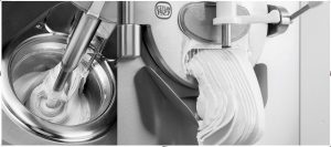 A commercial gelato machine churning creamy gelato, with the finished product being dispensed in thick, smooth ribbons from the spout into a container.
