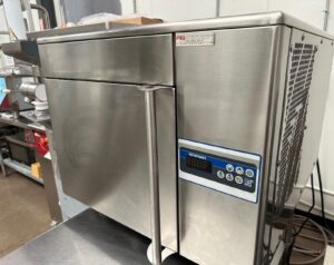A stainless steel commercial kitchen appliance with a digital control panel and buttons on the right side, sitting on a countertop in a professional kitchen setting.