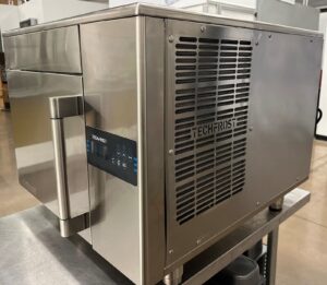 A stainless steel TECHFROST commercial blast chiller sits on a metal table in a professional kitchen, with digital control panel and ventilation grilles visible.