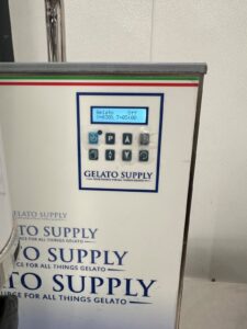 Close-up of a gelato machine control panel with a digital display showing Gelato Off and Unjog: T=0:15:00. The panel features several buttons and the label Gelato Supply.