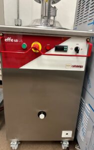 A commercial gelato machine with a red and white control panel labeled effe 6B and cattabriga. It has buttons, a display screen, and a turning knob, with a stainless steel body on wheels.
