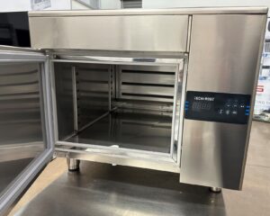 A stainless steel commercial oven with its door open, revealing the empty interior and metal shelves. The control panel on the right displays digital buttons and a small screen with the label TECH-ROST.
