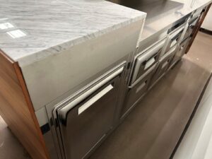 A close-up view of a modern kitchen with stainless steel cabinets and drawers, featuring a marble countertop and sleek, minimalist handles.