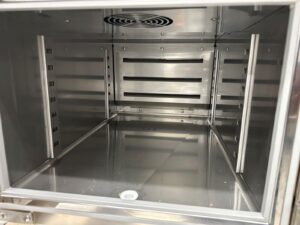 Interior of an empty stainless steel oven or commercial food warmer, showing metal racks and a vent at the back, with a clean, reflective surface.