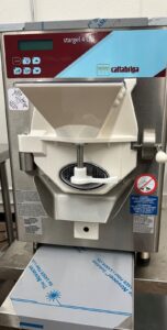 A Cattabriga Stargel 4 commercial gelato or ice cream maker with a digital control panel, white dispensing area, warning stickers, and a cardboard box positioned under the dispenser.